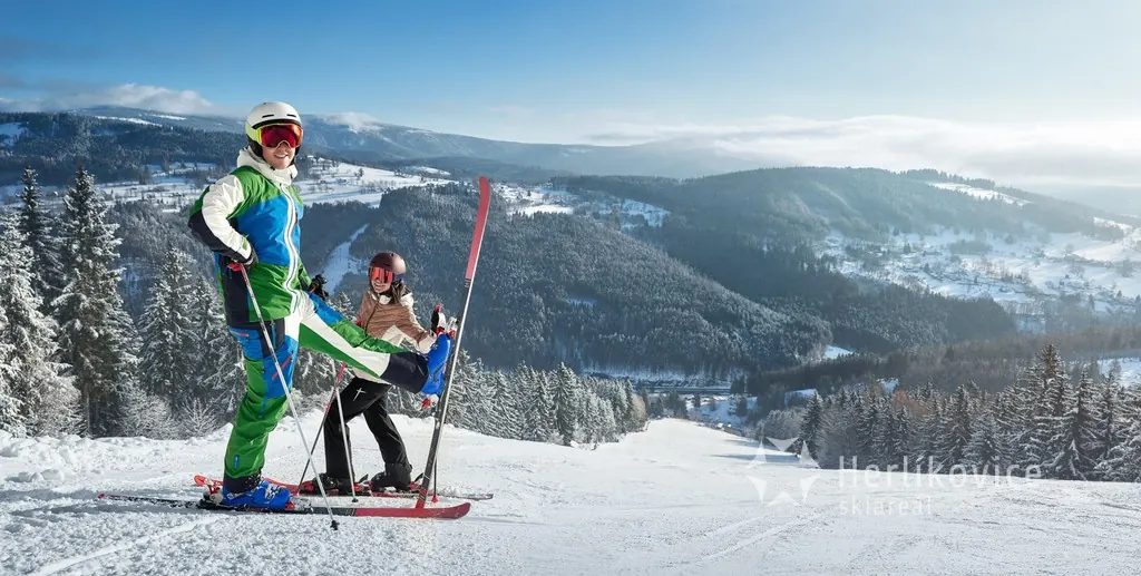 Lyžaři na vrcholu sjezdovky s výhledem do Krkonoš